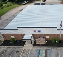 Aerial view of a VFW building with a metal roof, adjacent parking spaces, a flagpole, and a stone monument near the entrance.