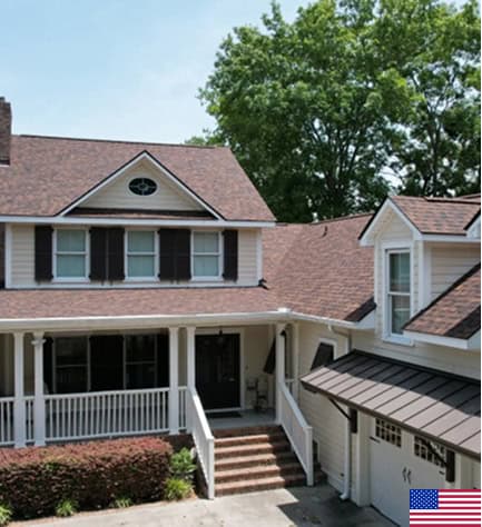 Two-story suburban house with beige siding, dark shutters, a covered front porch, and an attached garage; American flag icon in bottom right corner.