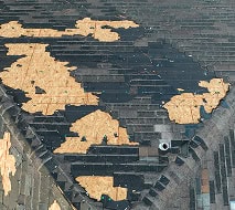 A roof with large patches of missing shingles, exposing the underlying wooden structure in several areas.