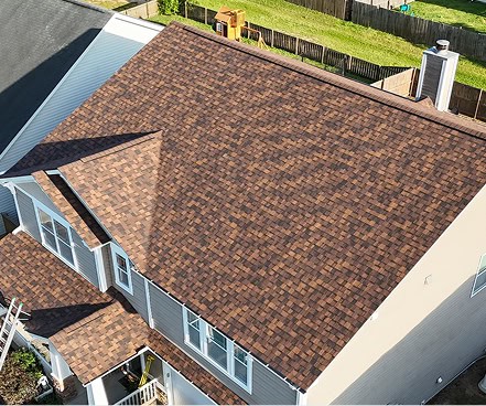 Aerial view of a house with a new brown shingle roof, white trim, and visible backyard with green grass and a wooden fence.