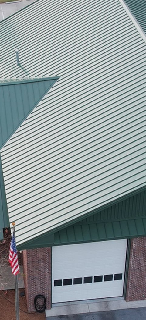 A green metal roof covers a brick building with a white garage door; an American flag is visible in the lower left corner.