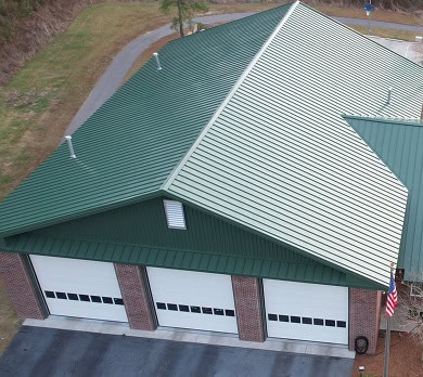 Aerial view of a green-roofed brick building with four large white garage doors and an American flag at the front.