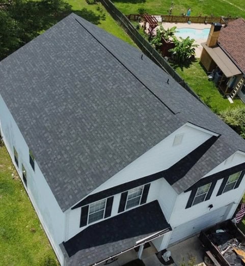 Aerial view of a two-story white house with a dark gray shingled roof, surrounded by grass, a fence, and a backyard with a swimming pool.