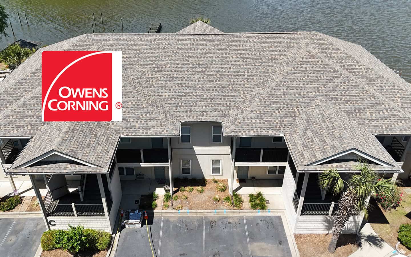 Aerial view of a multi-unit residential building with a newly installed shingle roof; Owens Corning logo displayed in the top left corner.