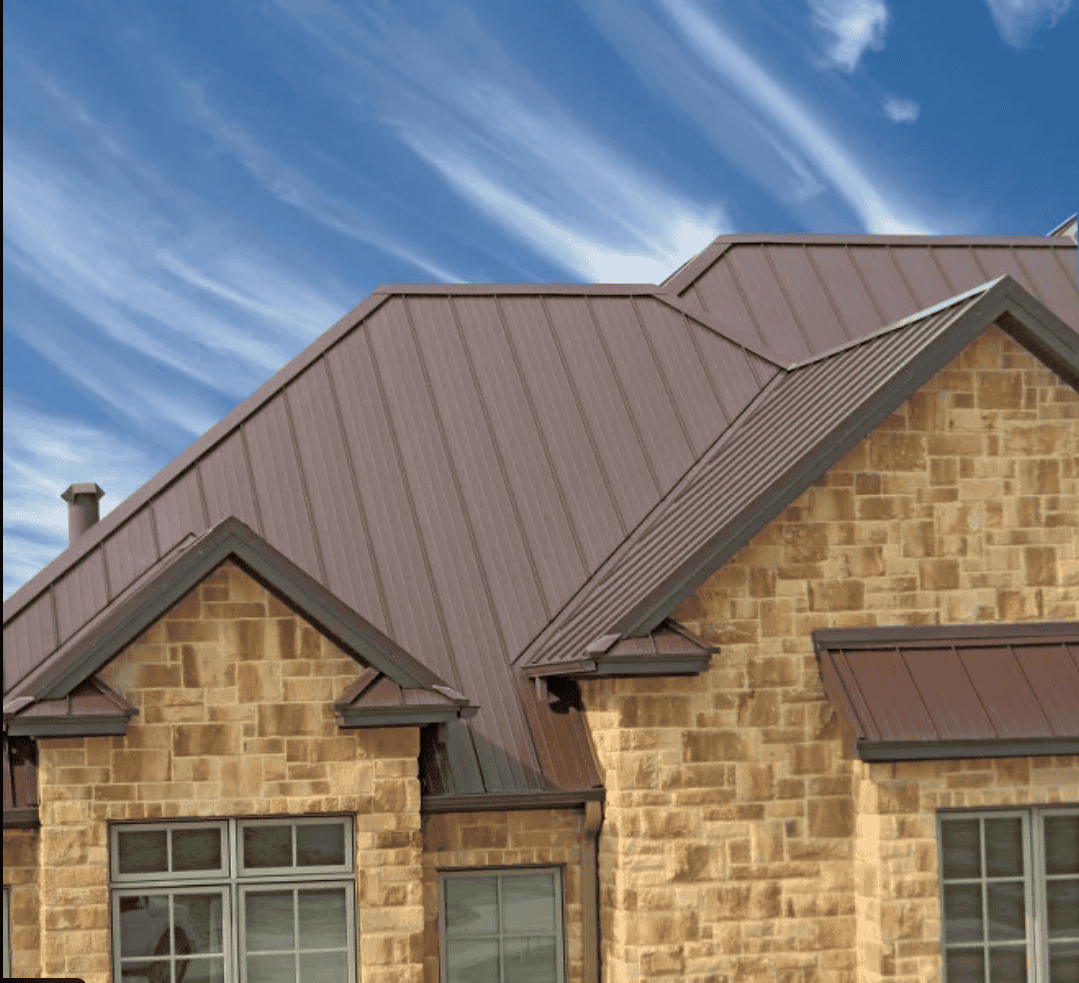 Stone house with brown metal roof under a blue sky with wispy clouds.