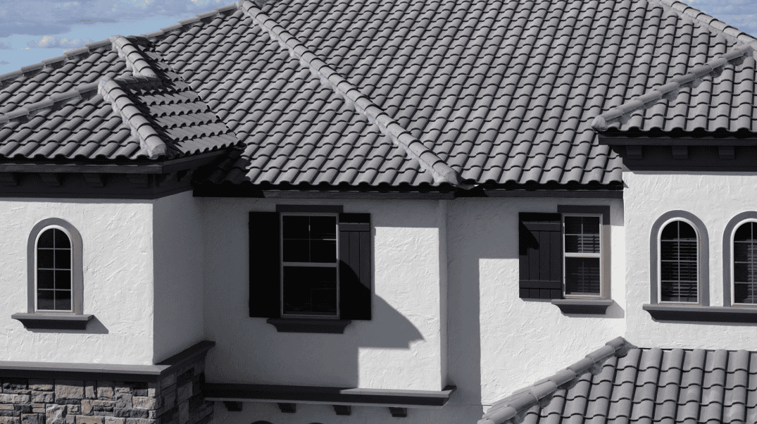 A house with a gray tile roof, white stucco walls, arched and rectangular windows, and black shutters.